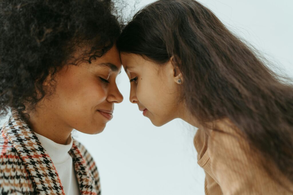 The power of cultural continuity. An adult and a child stand close together with their foreheads touching, both with eyes closed and calm expressions.