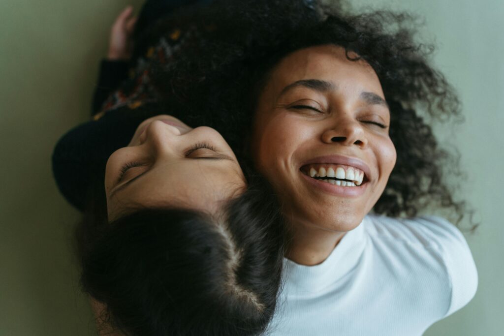 one women and female teenager smiling joyfully, heads resting together, celebrating foster care awareness month and the joy of supporting children in care.