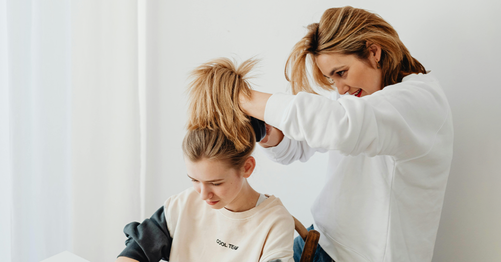 A foster mom styles a girl's hair in a bright, cozy home, illustrating daily care and support in foster care.