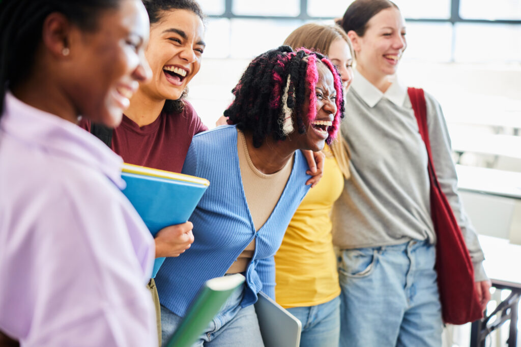 A group of five diverse students laughing together, holding books and notebooks. Conveying friendship.